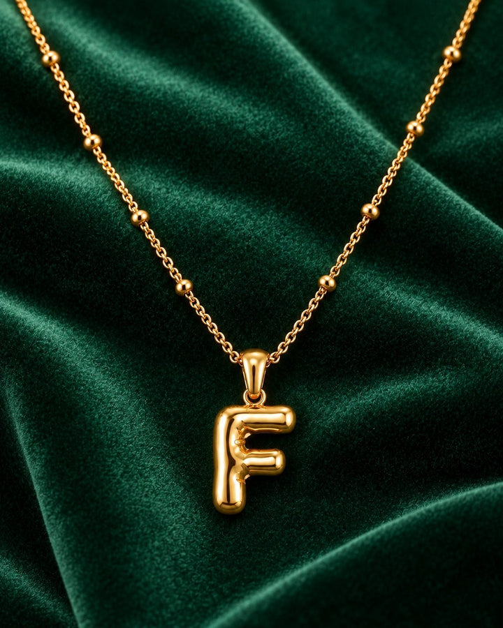 Elli Jewellery gold plated chunky initial F pendant necklace on a dark green velvet background