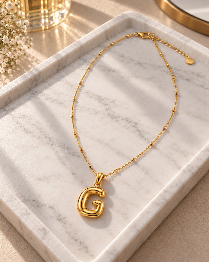Elli Jewellery gold plated chunky initial G pendant necklace on a white marble tray with delicate beaded chain detail
