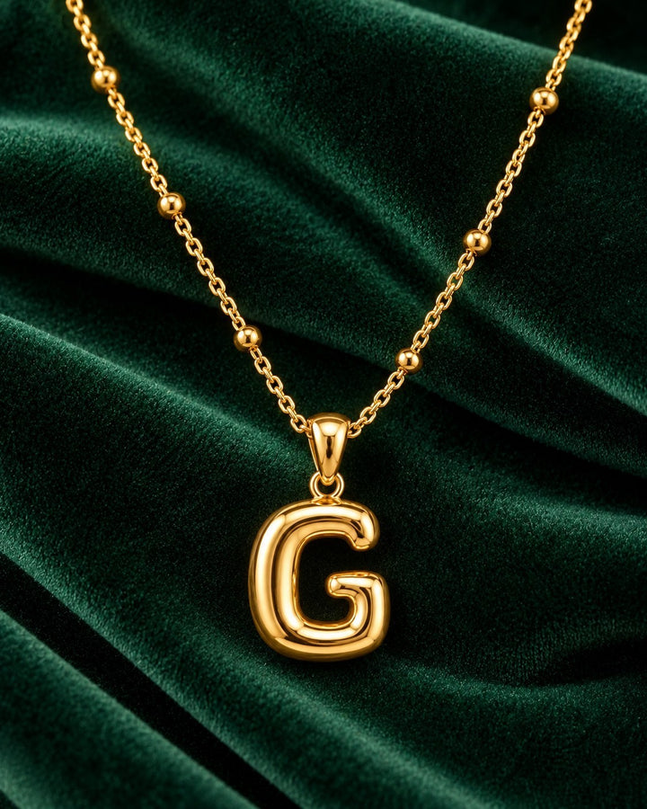 Elli Jewellery gold plated chunky chain necklace featuring a bold initial G pendant on a dark green velvet background