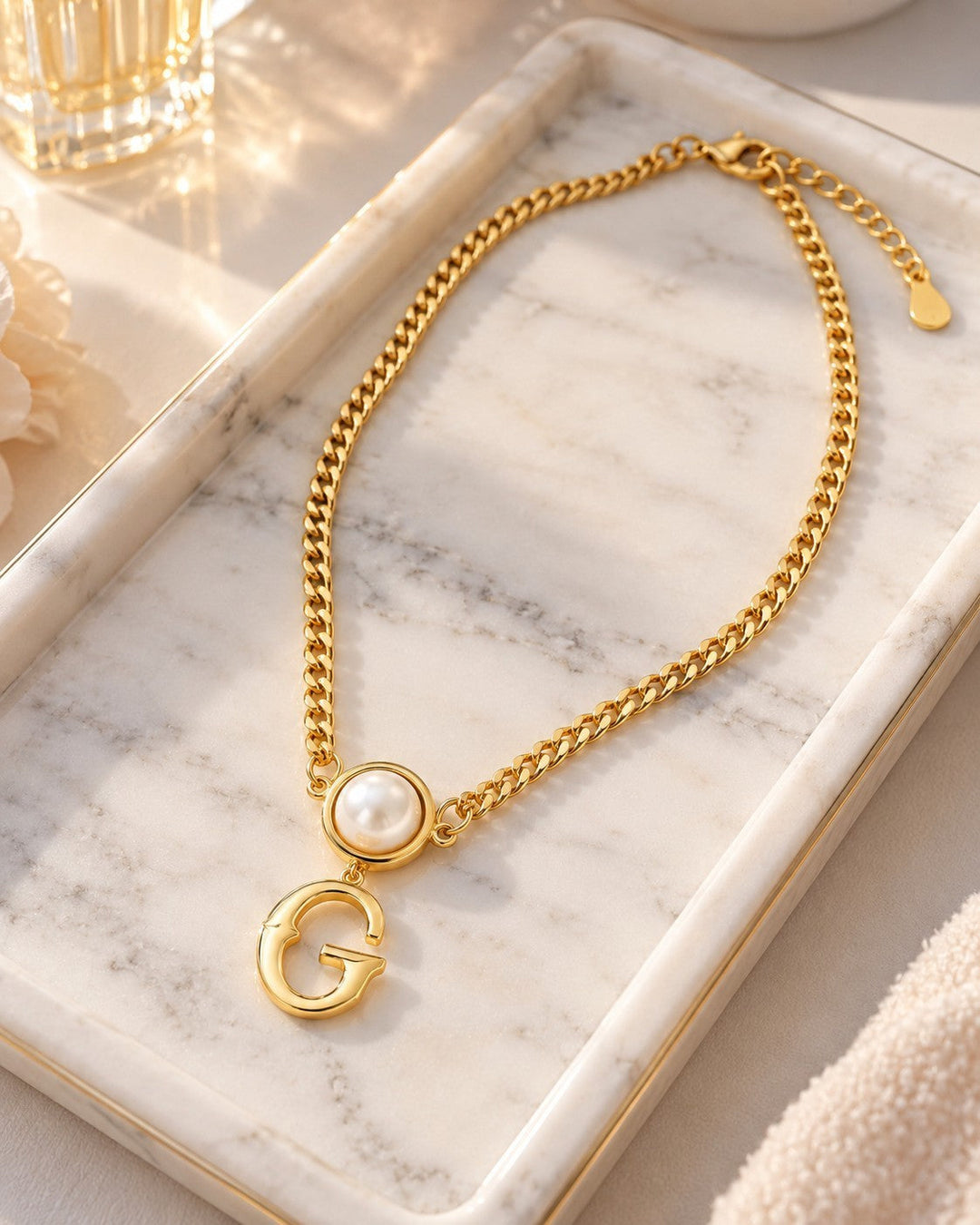 Elli Jewellery gold plated curb chain necklace featuring a pearl accent and a bold letter G pendant on marble tray.