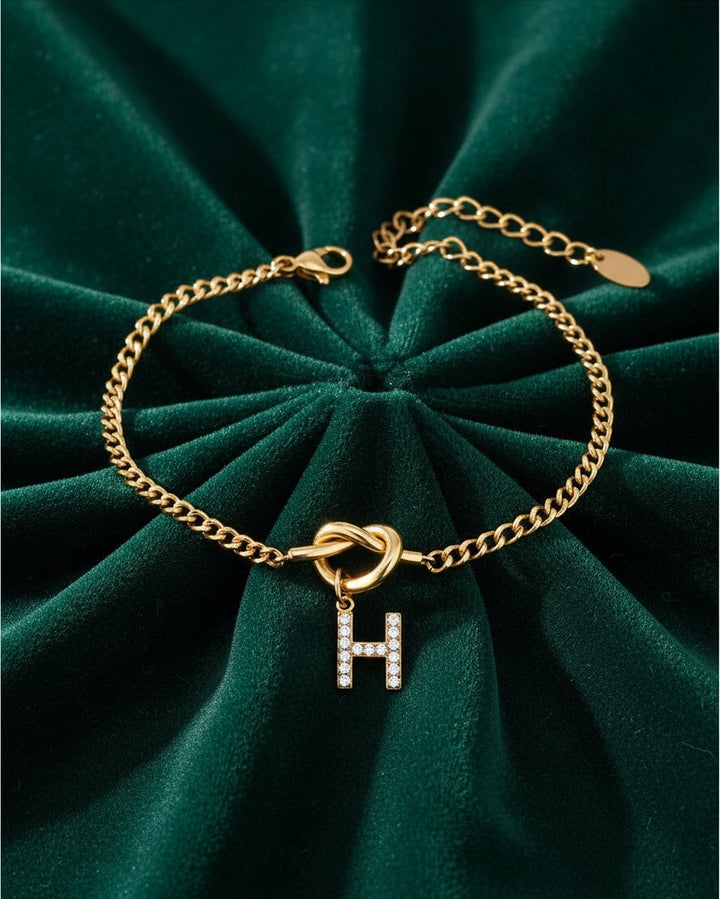Elli Jewellery gold-plated chain bracelet featuring a diamante-encrusted letter H charm on a green velvet background.