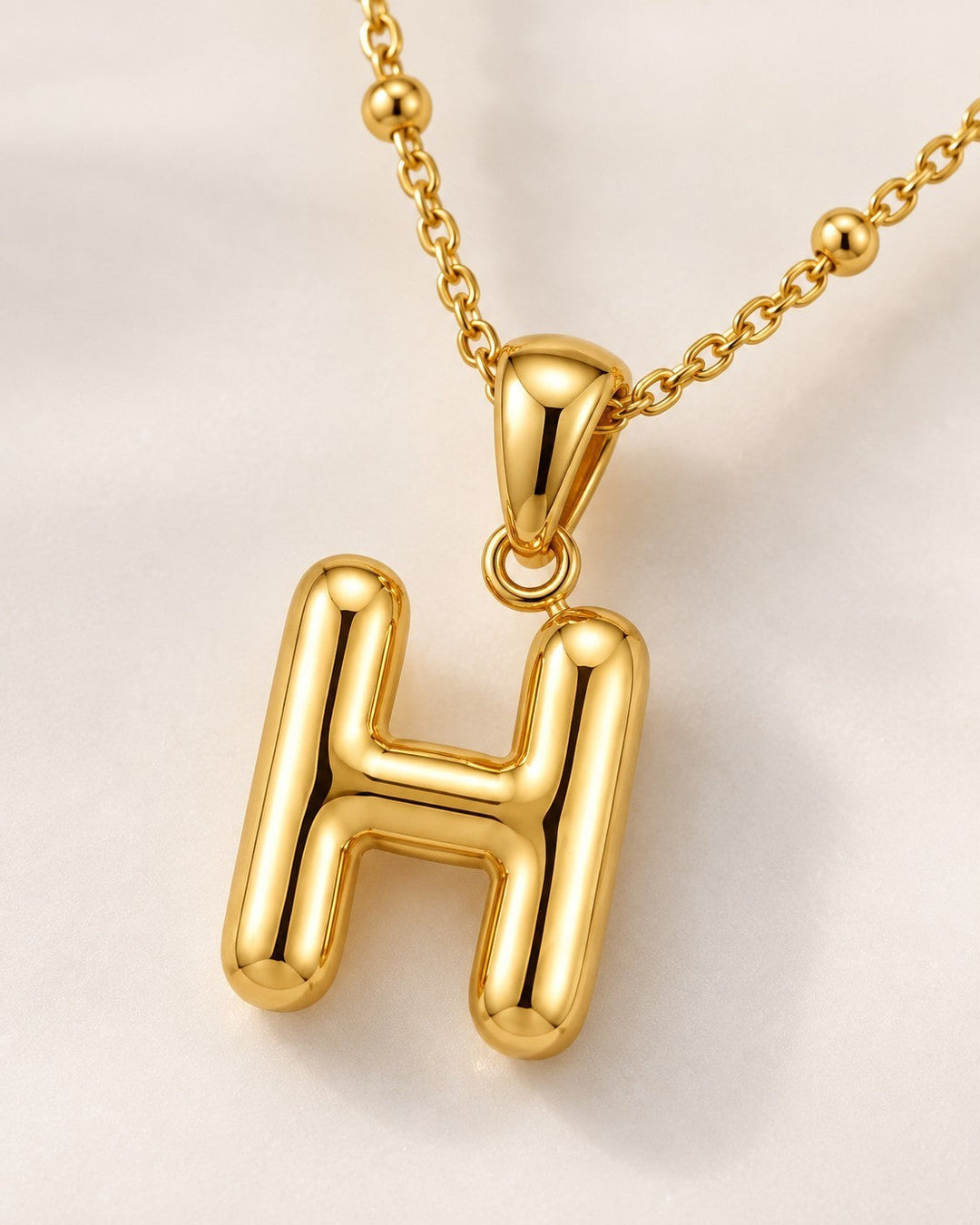 Elli Jewellery gold plated chunky initial H pendant necklace on a delicate beaded chain against a white background