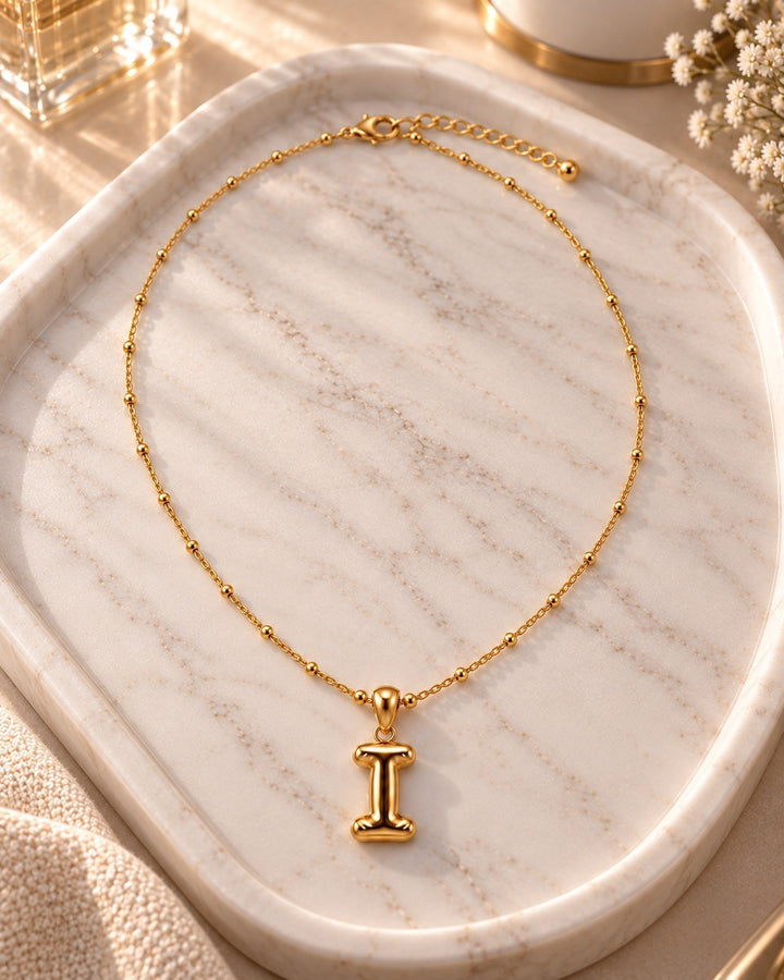 Elli Jewellery gold plated waterproof initial I pendant necklace with a delicate beaded chain on a marble tray.