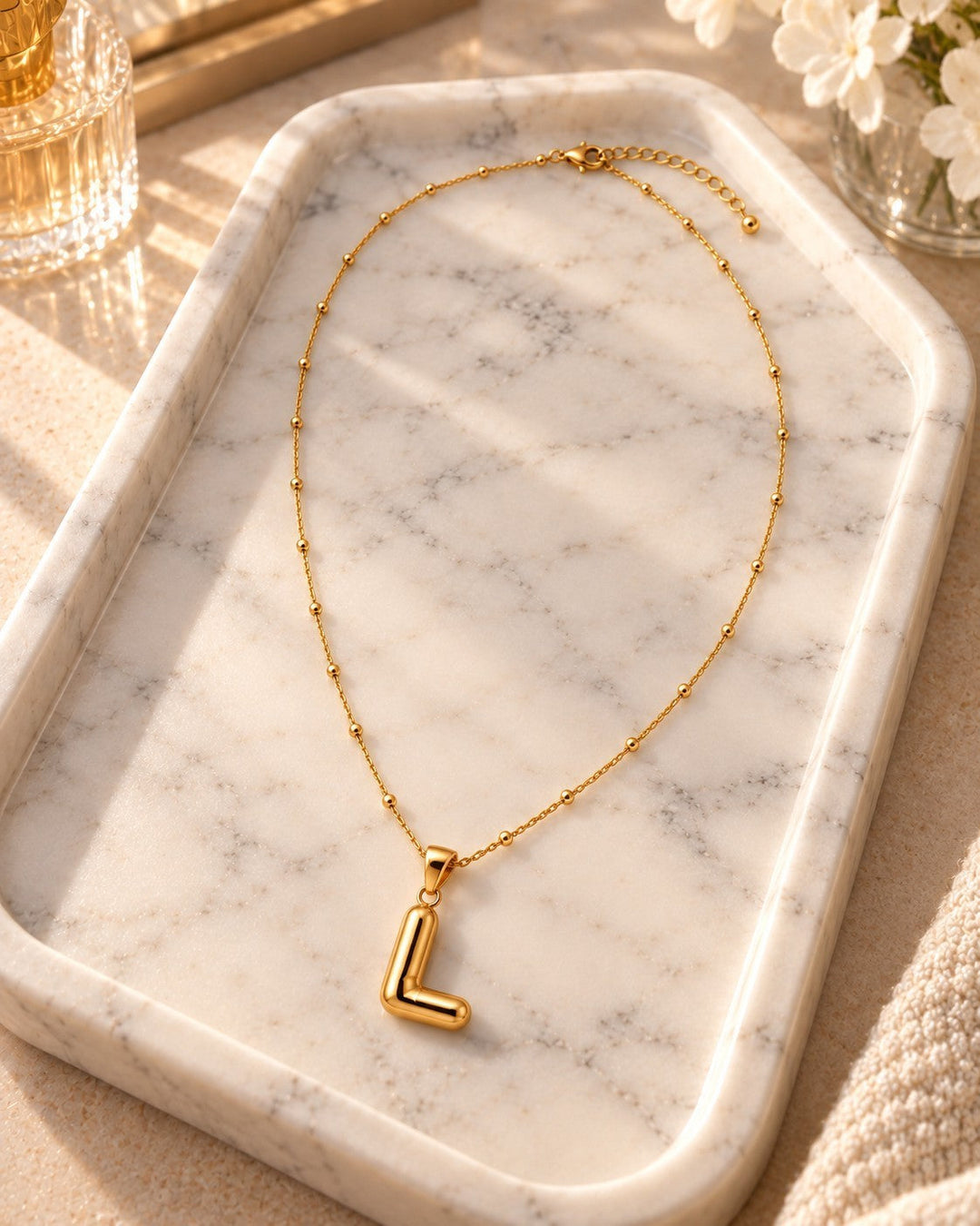 Elli Jewellery gold plated initial L pendant necklace on a delicate beaded chain resting on a marble tray.