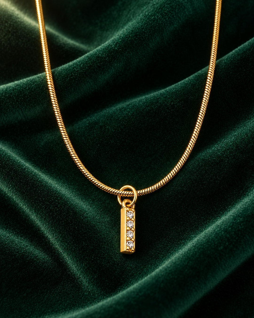 Elli Jewellery gold plated waterproof initial I pendant necklace with small crystals on a dark green velvet background