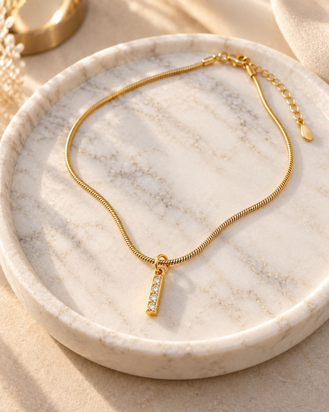 Elli Jewellery gold plated waterproof initial I pendant necklace with crystal accents on a marble tray