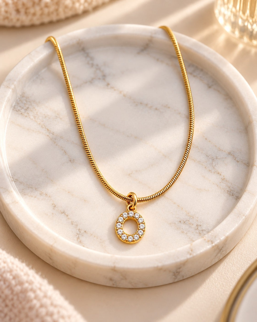 Elli Jewellery gold plated waterproof initial O pendant necklace with crystal accents on a marble tray