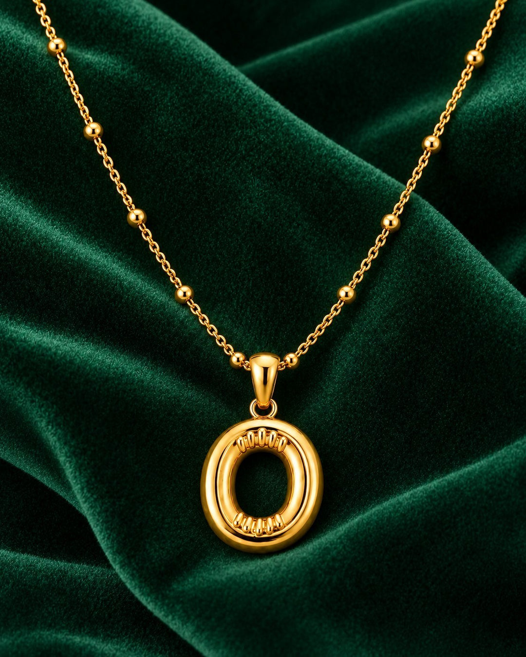 Elli Jewellery gold plated chunky initial O pendant necklace on a dark green velvet background