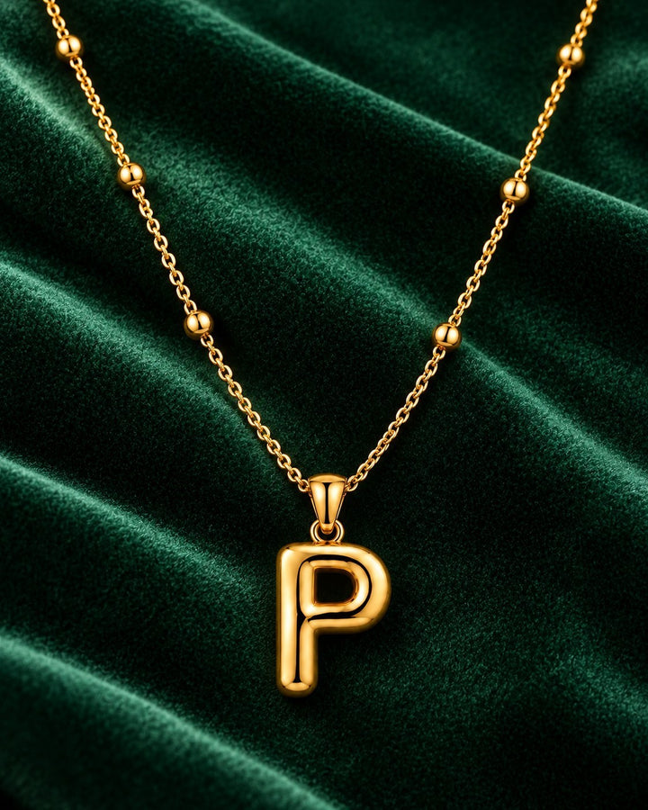 Elli Jewellery gold plated chunky initial P pendant necklace on a beaded chain against a dark green velvet background