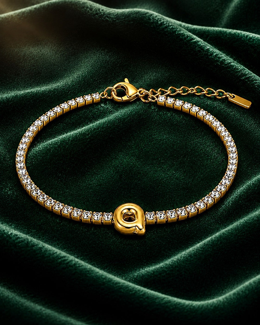 Elli Jewellery gold plated waterproof initial Q charm bracelet with sparkling crystal accents on green velvet.