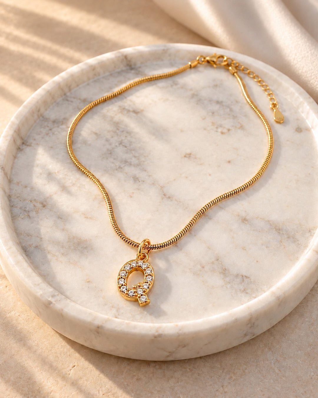 Elli Jewellery gold plated waterproof initial Q pendant necklace with crystal accents on a marble tray