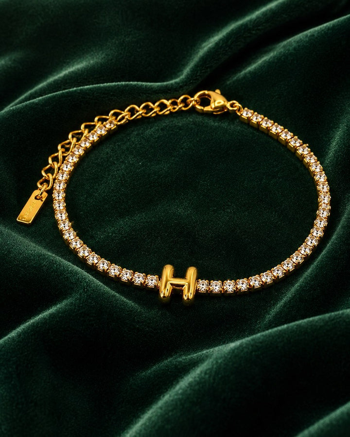 Elli Jewellery gold plated tennis bracelet featuring a letter H initial charm on a green velvet background