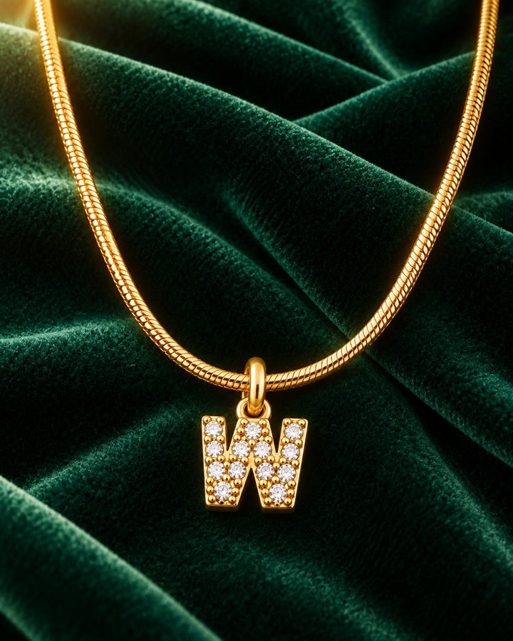 Elli Jewellery gold plated initial W pendant necklace with sparkling crystals on a green velvet background