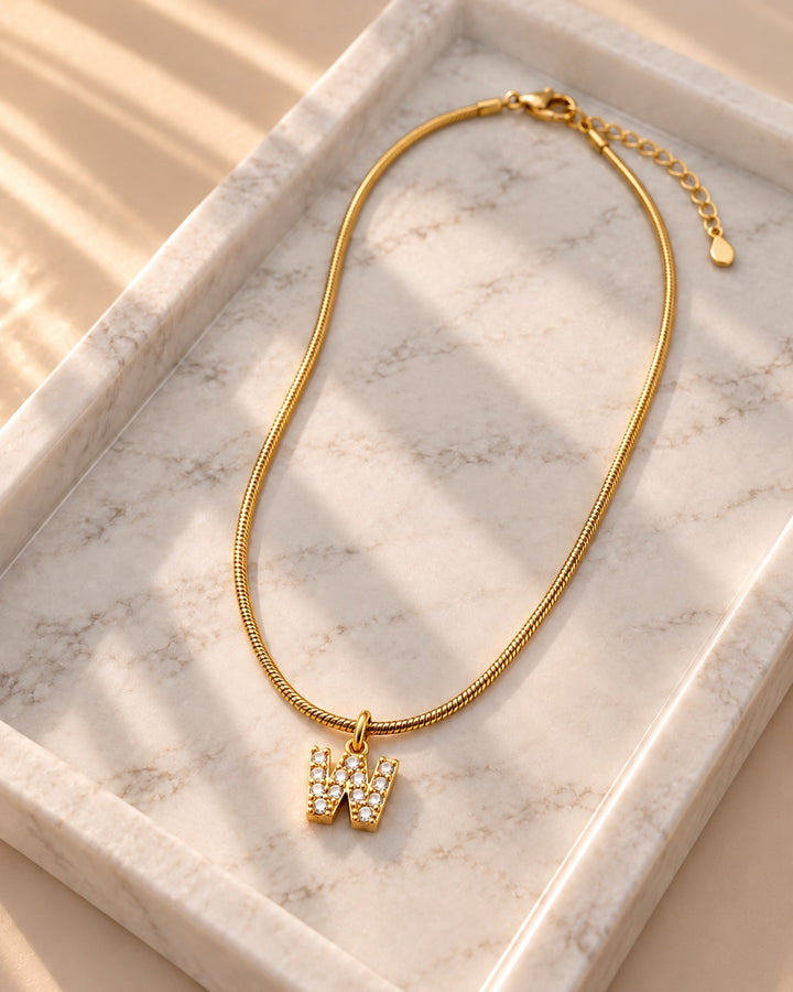 Elli Jewellery gold plated waterproof initial W pendant necklace with sparkling stones on a marble tray