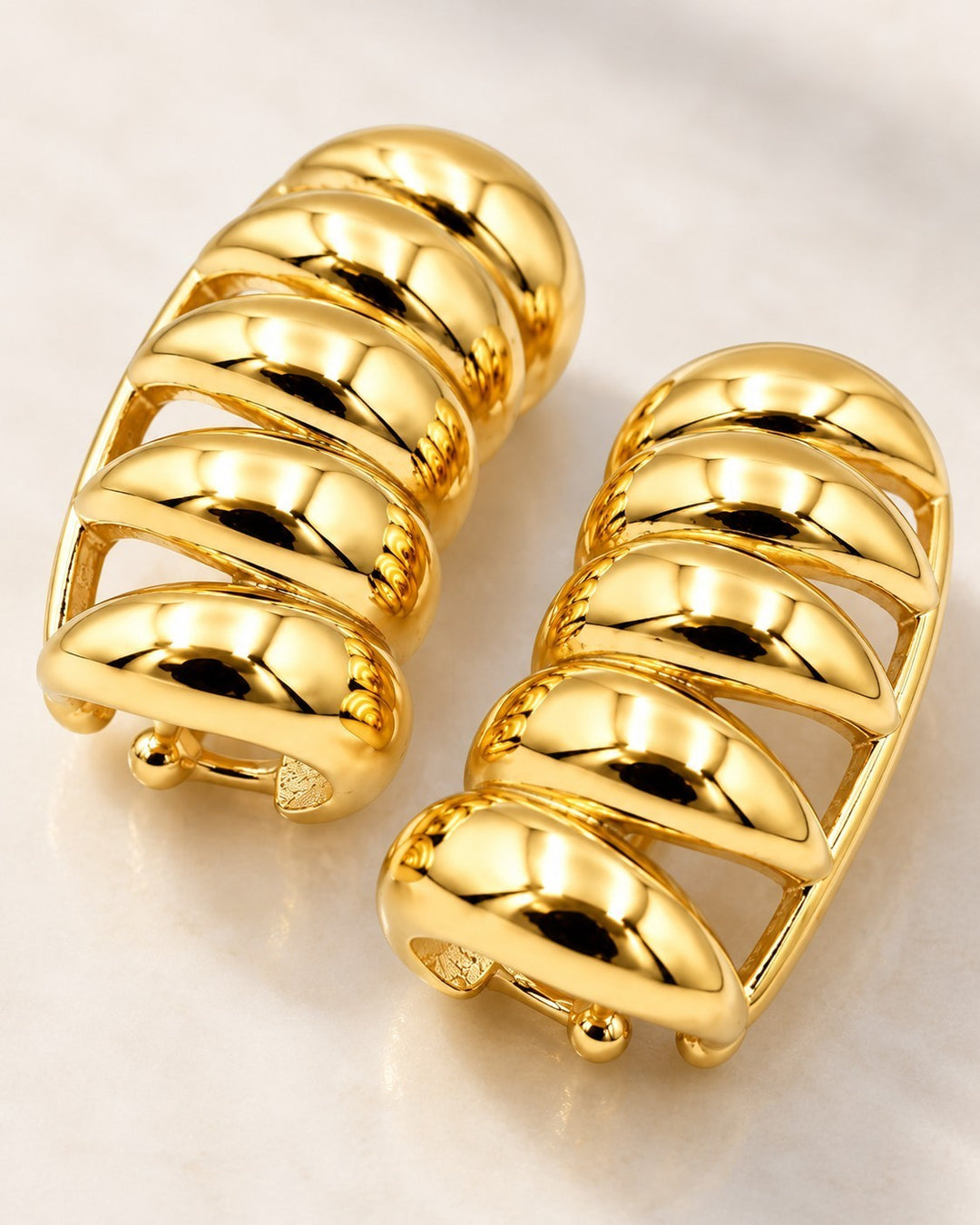 Elli Jewellery gold plated multi-layer insect charm stud earrings with a polished finish on a marble surface