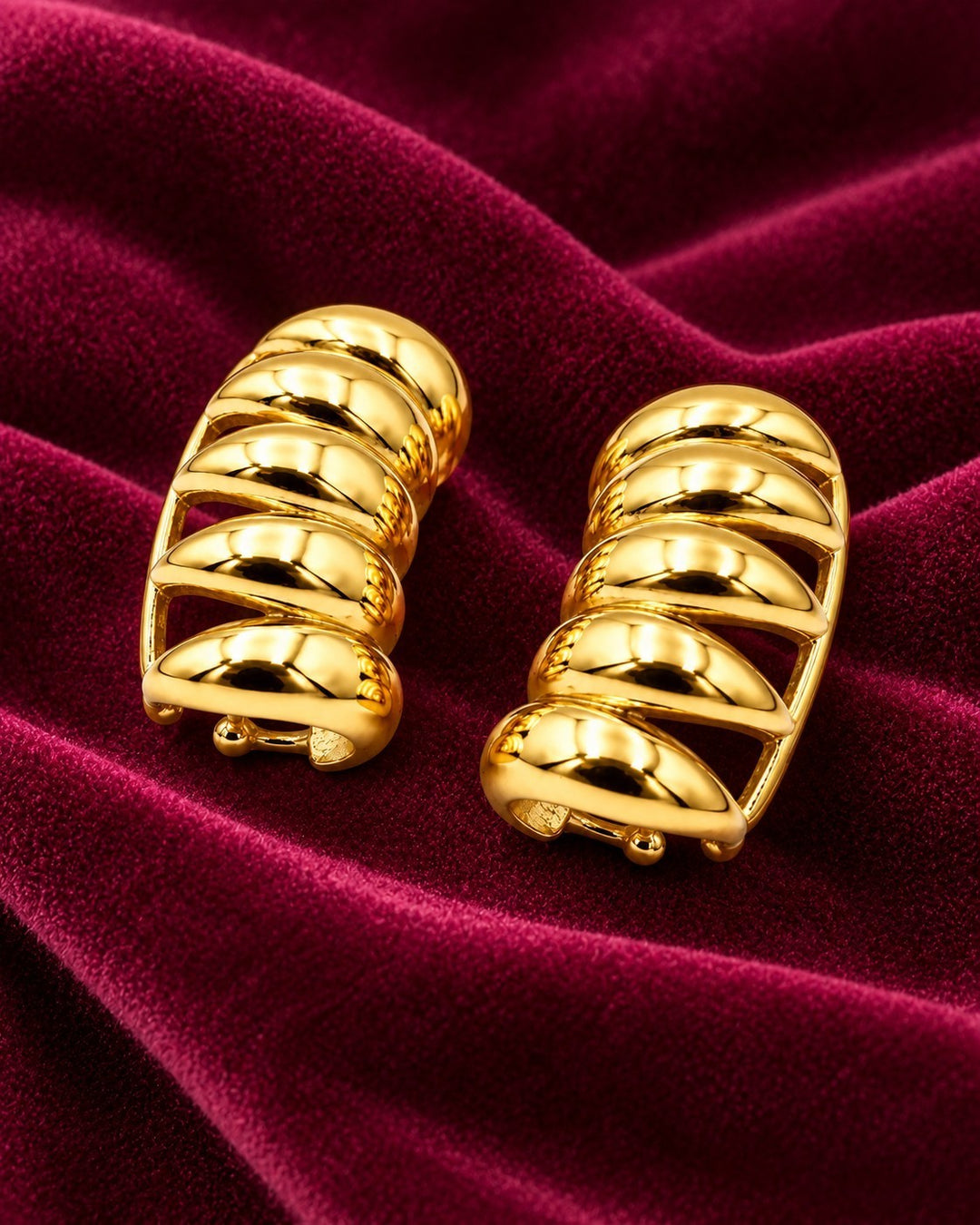 Elli Jewellery gold plated multi-layer insect charm stud earrings resting on a deep red velvet fabric background.