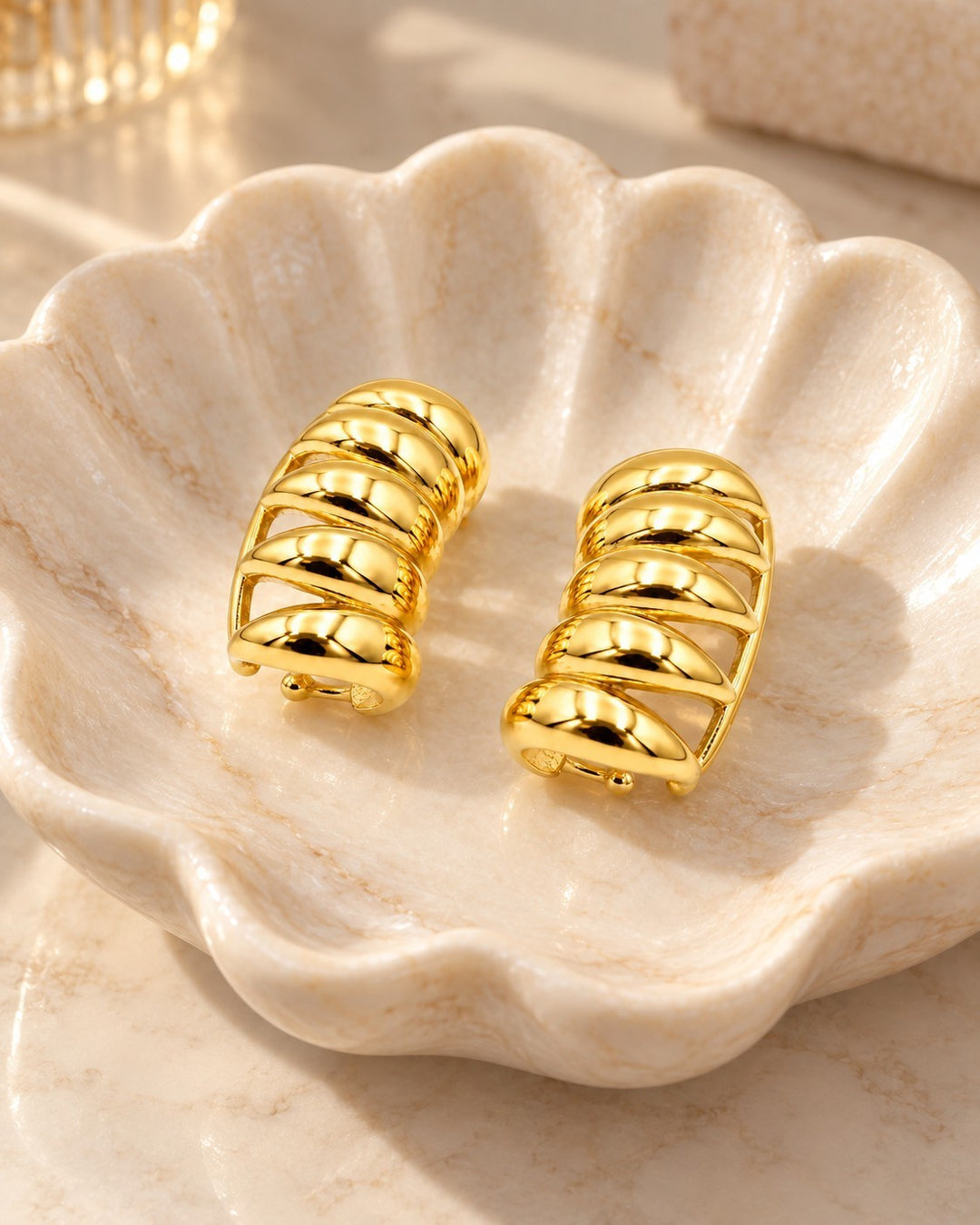 Elli Jewellery gold plated multi-layer insect charm stud earrings resting in a decorative shell dish.