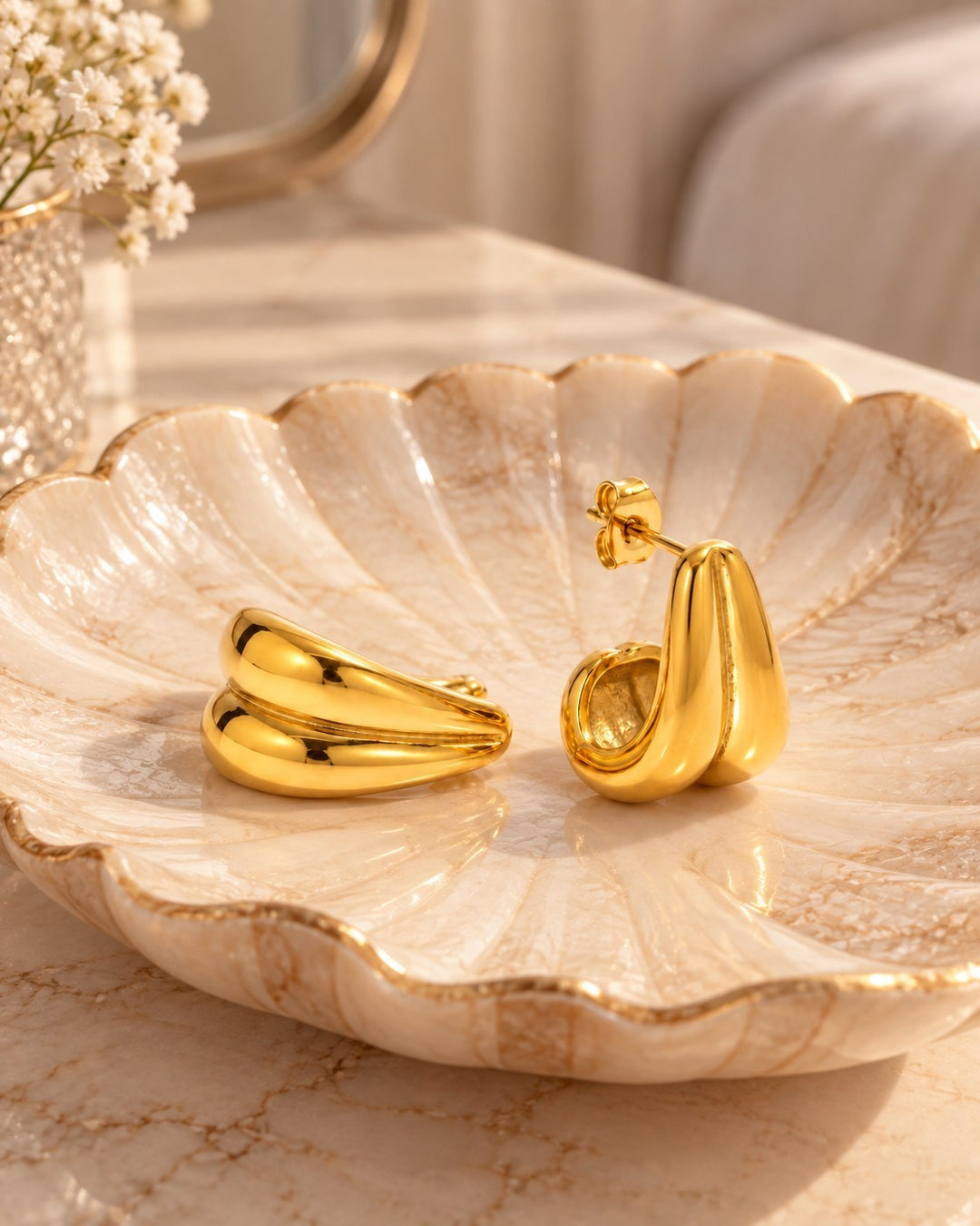Elli Jewellery gold plated stainless steel interlocking double C hoop earrings resting on a decorative shell dish.
