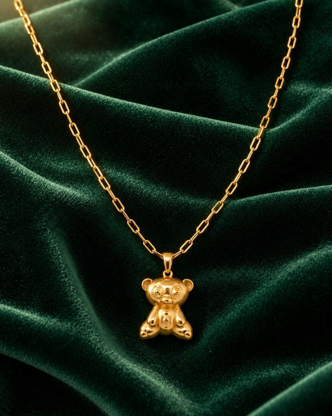 Elli Jewellery gold plated koala bear pendant on a delicate chain resting on a luxurious dark green velvet background.