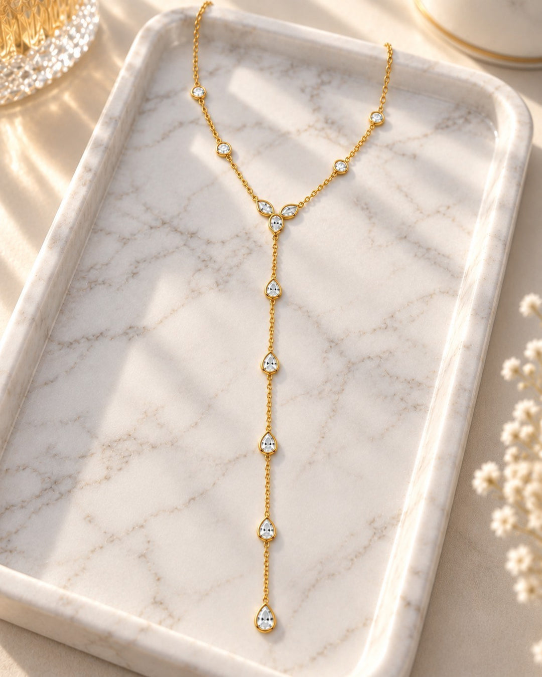 Elli Jewellery gold plated lariat necklace with teardrop crystals on a marble tray, minimalist waterproof design.