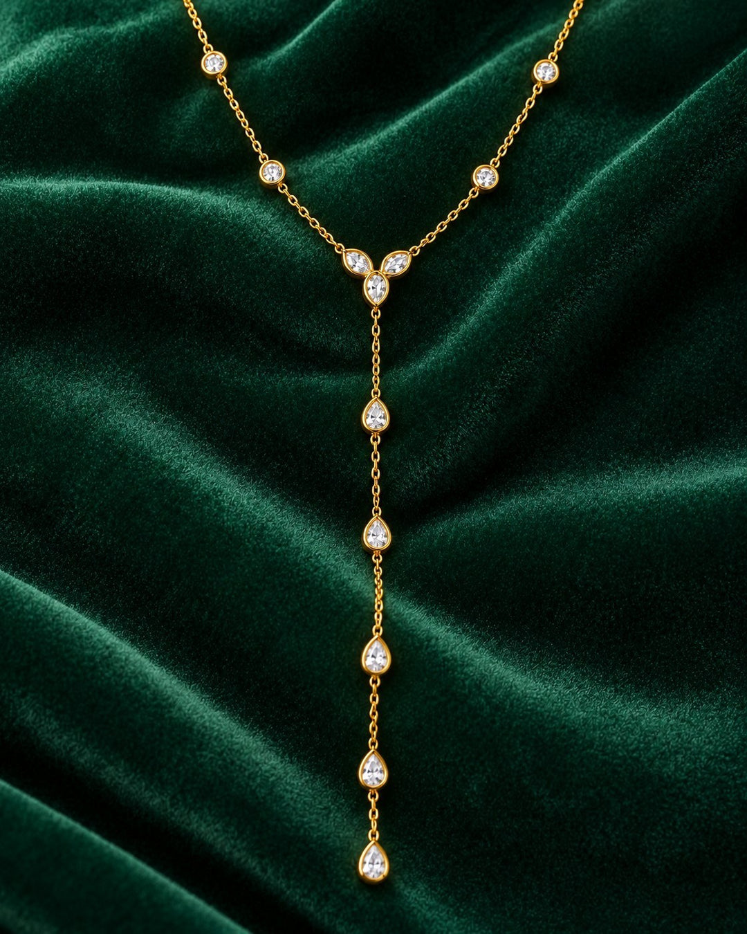 Elli Jewellery gold plated lariat necklace with teardrop and round crystals on a dark green velvet background