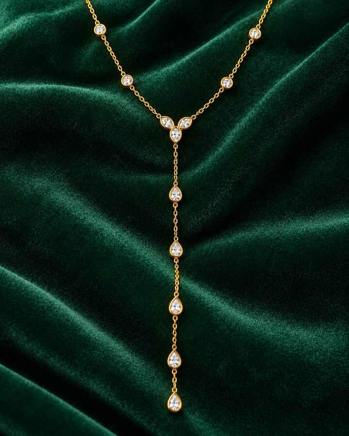Elli Jewellery gold plated lariat necklace with teardrop and round crystals on a dark green velvet background