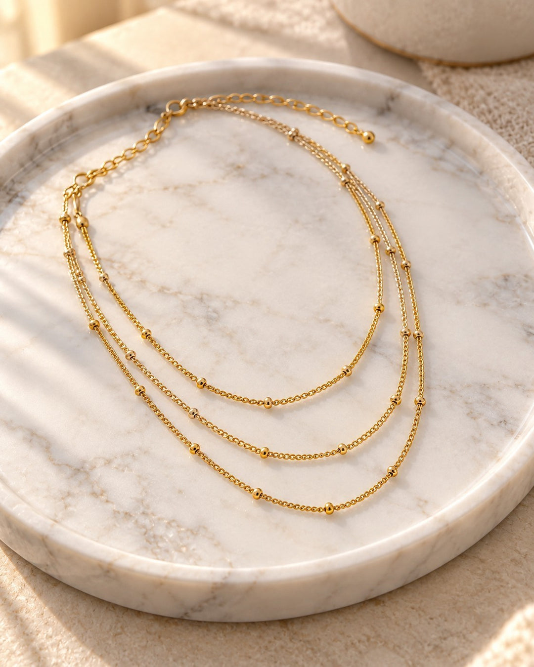 Elli Jewellery gold plated triple layered chain necklace with delicate beads on a marble tray