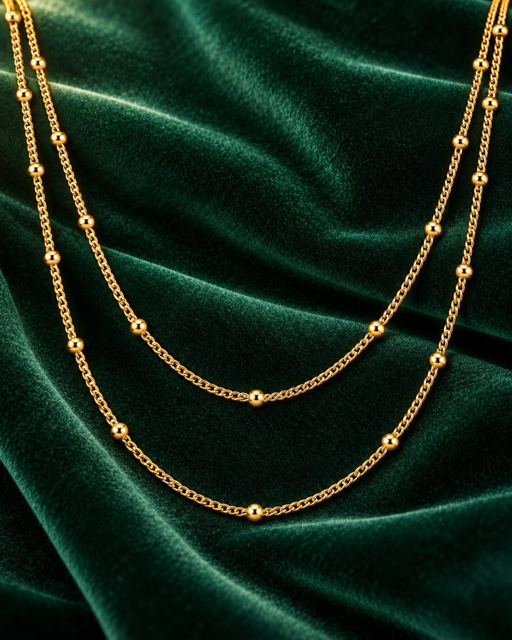 Elli Jewellery gold plated triple layered beaded chain necklace on a dark green velvet background