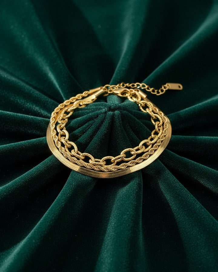 Elli Jewellery gold-plated layered chain bracelet featuring a herringbone and rope chain design on green velvet.
