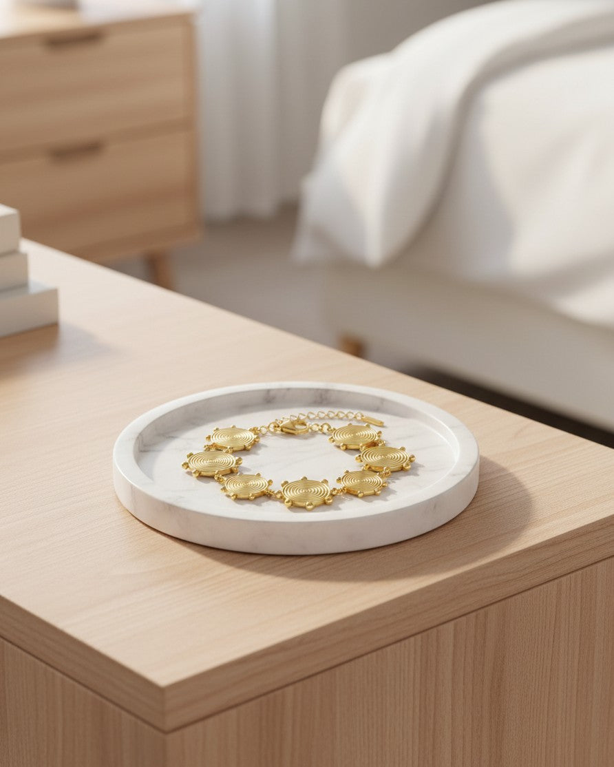 Elli Jewellery gold plated layered charm dangle bracelet resting on a white marble tray on a wooden bedside table.