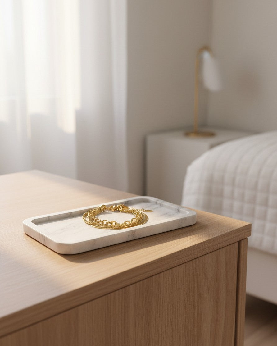 Elli Jewellery gold-plated multi-charm layered chain bracelet resting on a white marble tray on a wooden bedside table.