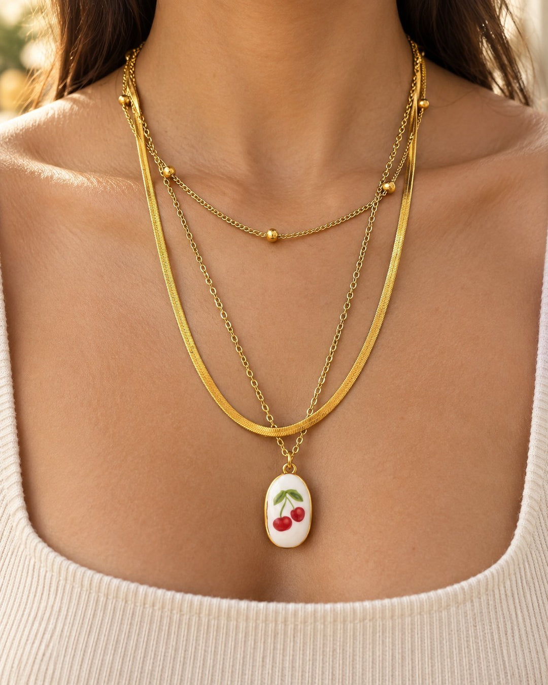 Elli Jewellery gold-plated layered snake chain necklace featuring a white oval pendant with a red cherry charm design.