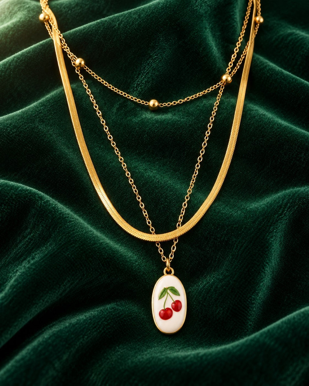 Elli Jewellery gold-plated layered snake chain necklace featuring a delicate cherry charm on a dark green velvet cloth