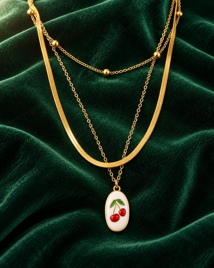 Elli Jewellery gold-plated layered snake chain necklace featuring a delicate cherry charm on a dark green velvet cloth