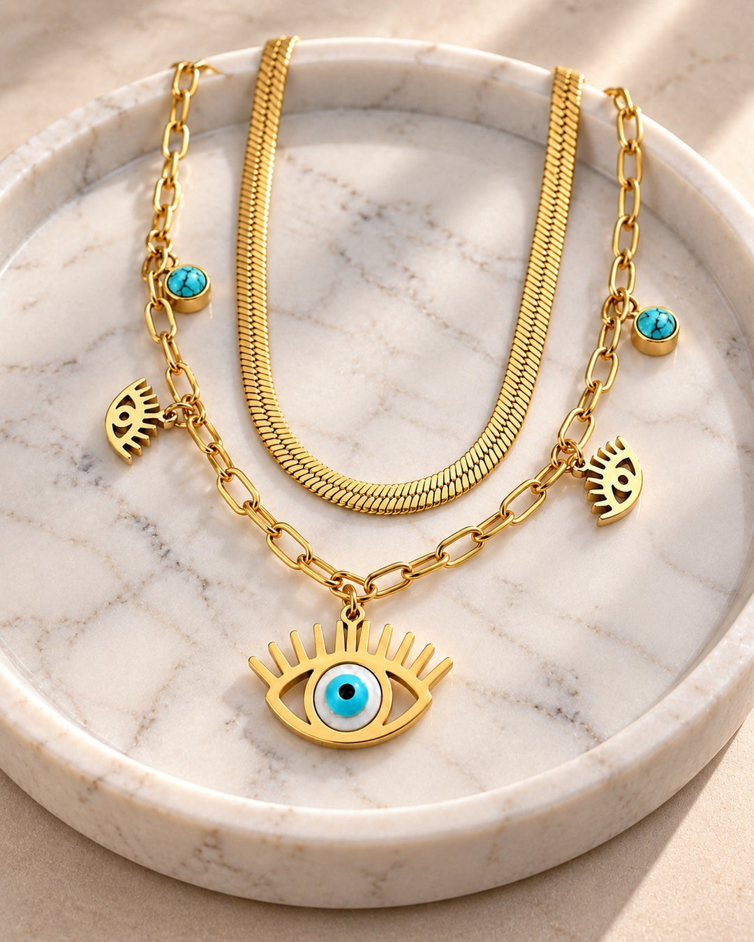 Elli Jewellery gold plated layered necklace featuring a snake chain, paperclip chain, and evil eye charms on marble