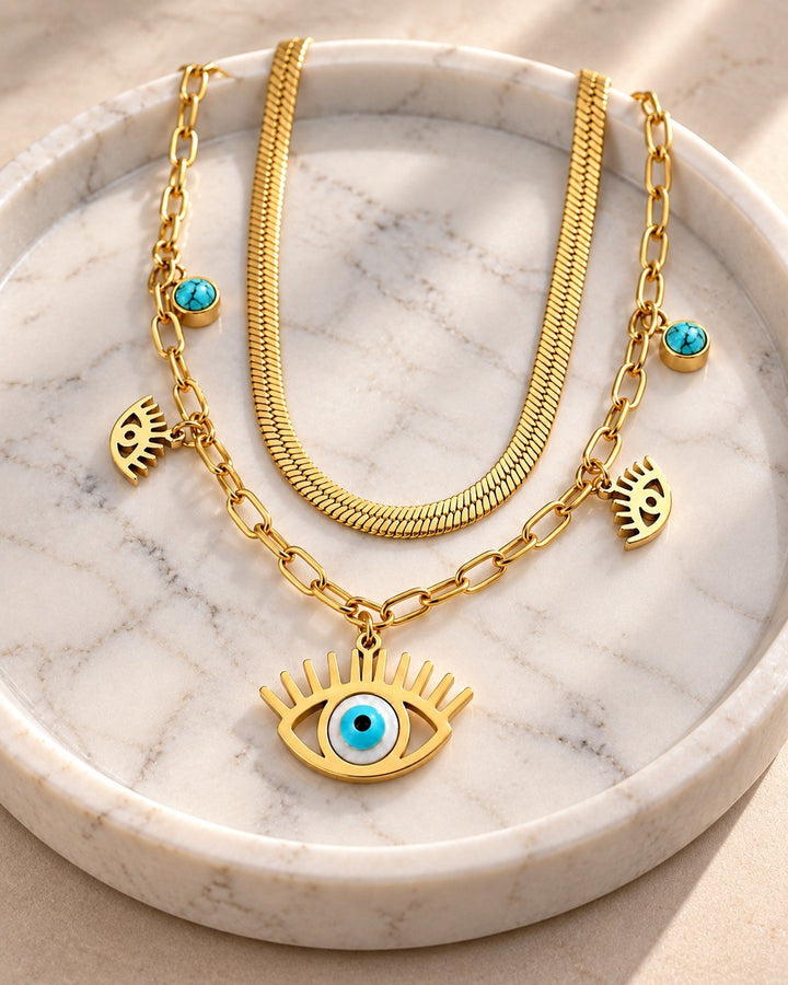 Elli Jewellery gold plated layered necklace featuring a snake chain, paperclip chain, and evil eye charms on marble