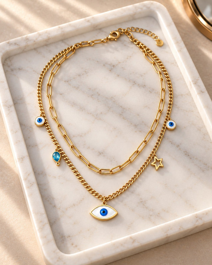 Elli Jewellery gold plated layered necklace with paperclip chain, evil eye charms, and star pendant on marble tray.