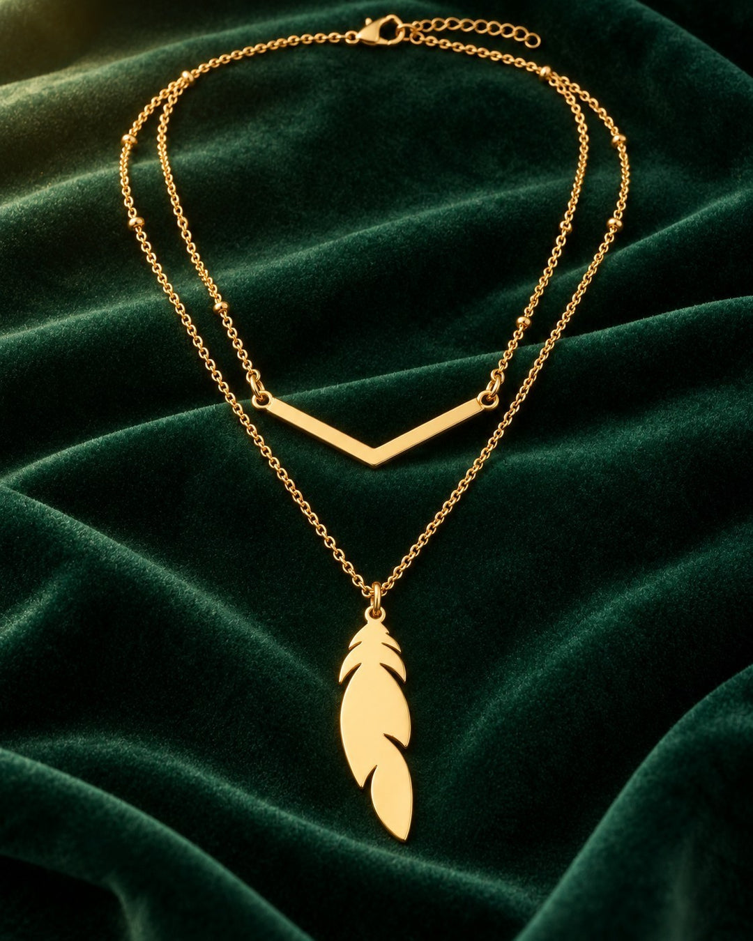 Elli Jewellery gold plated layered necklace with a delicate leaf charm and v-shaped bar on a dark green velvet cloth.
