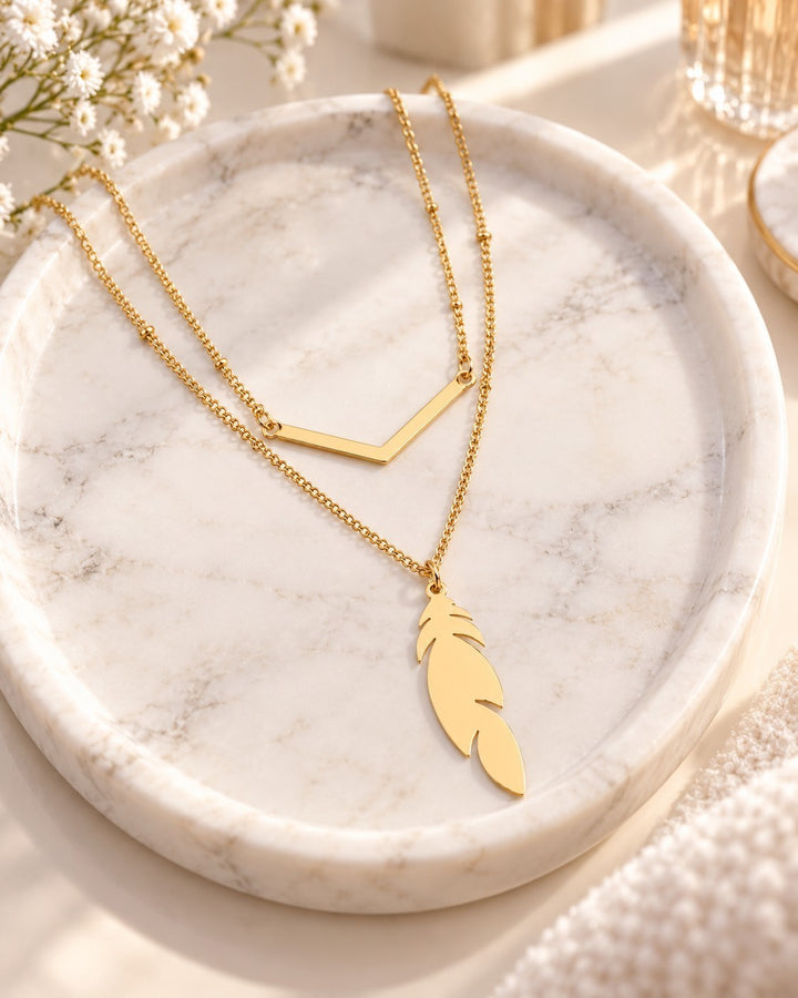 Elli Jewellery gold plated layered necklace with a delicate leaf charm and V-shaped bar on a marble tray.
