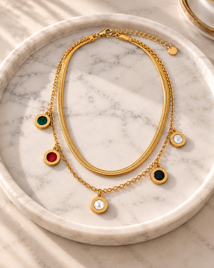 Elli Jewellery gold plated layered snake chain necklace with multicoloured circular charms on a marble tray
