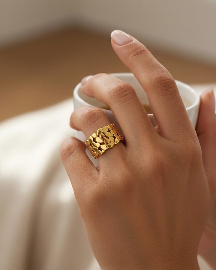 Elli Jewellery gold plated band ring featuring a delicate hollow leaf pattern worn on a finger holding a white cup.