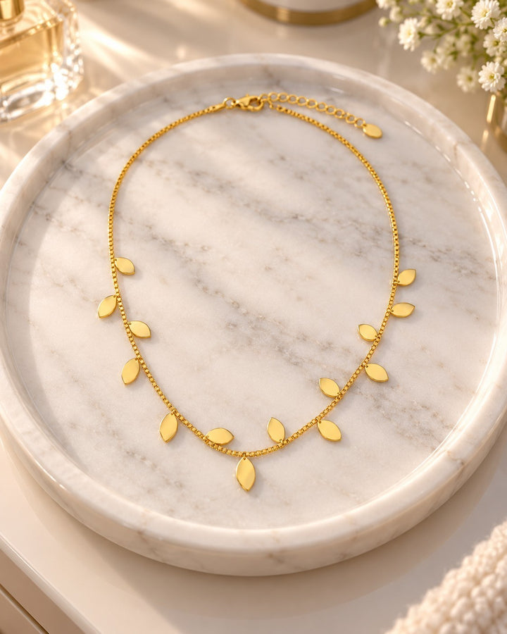 Elli Jewellery gold plated botanical leaf necklace with delicate chain charms on a marble tray
