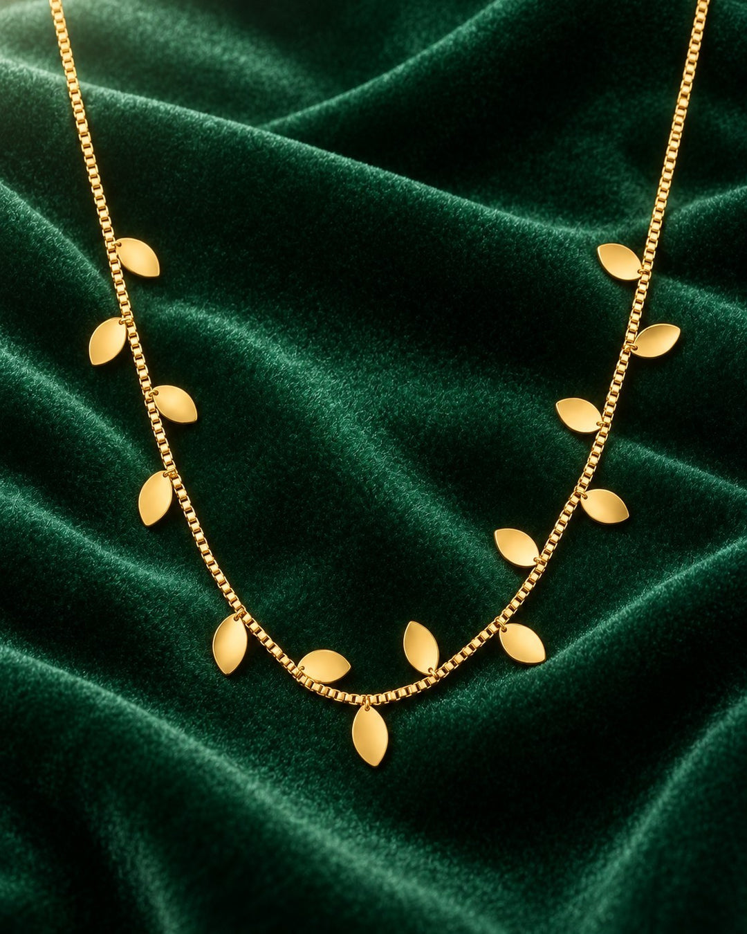 Elli Jewellery gold plated botanical leaf statement necklace on a dark green velvet background.
