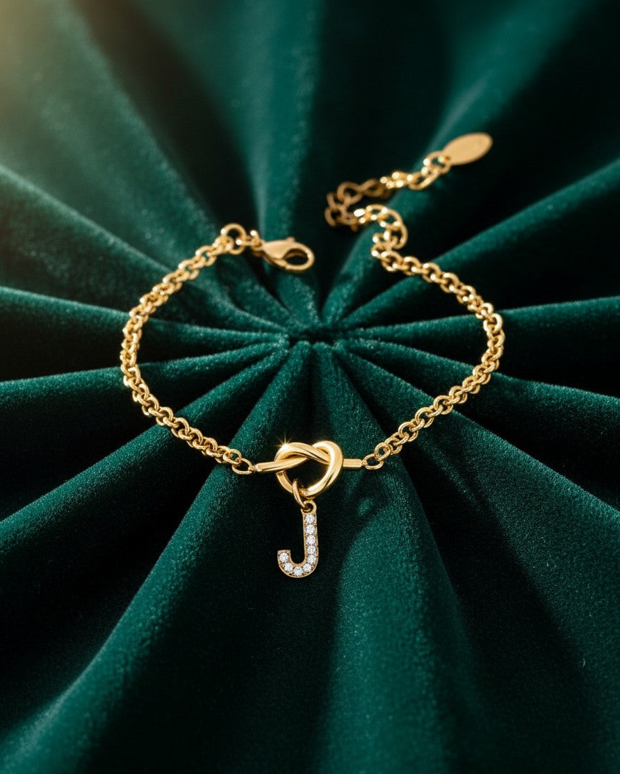Elli Jewellery gold plated chain bracelet featuring a crystal-embellished letter J charm on a green velvet background