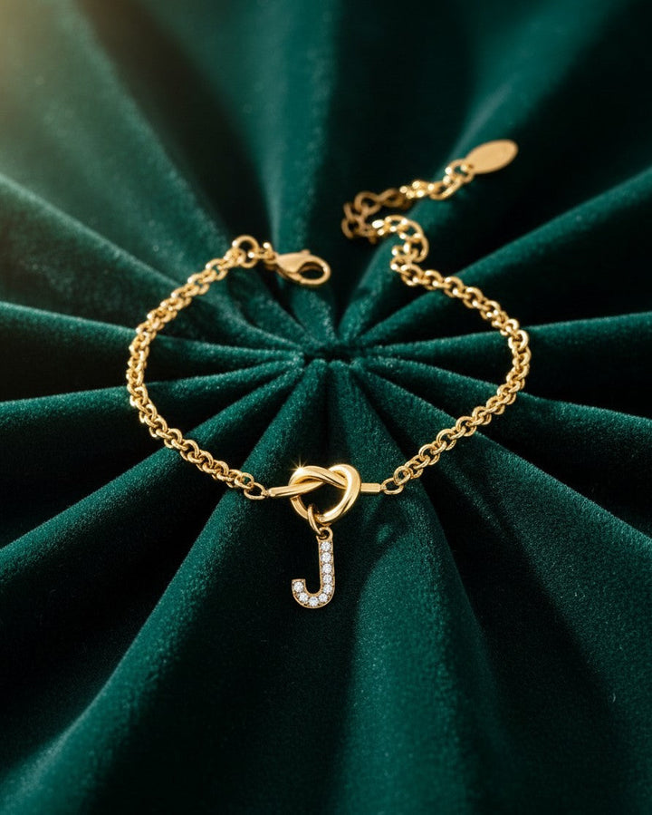 Elli Jewellery gold plated chain bracelet featuring a crystal-embellished letter J charm on a green velvet background