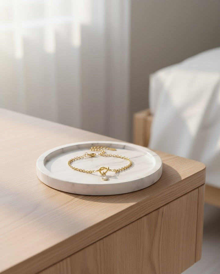 Elli Jewellery gold plated chain bracelet with a crystal letter J charm resting on a white marble tray.