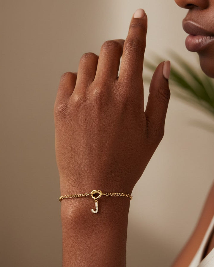 Elli Jewellery gold plated chain bracelet featuring a sparkling crystal letter J initial charm on a model's wrist.