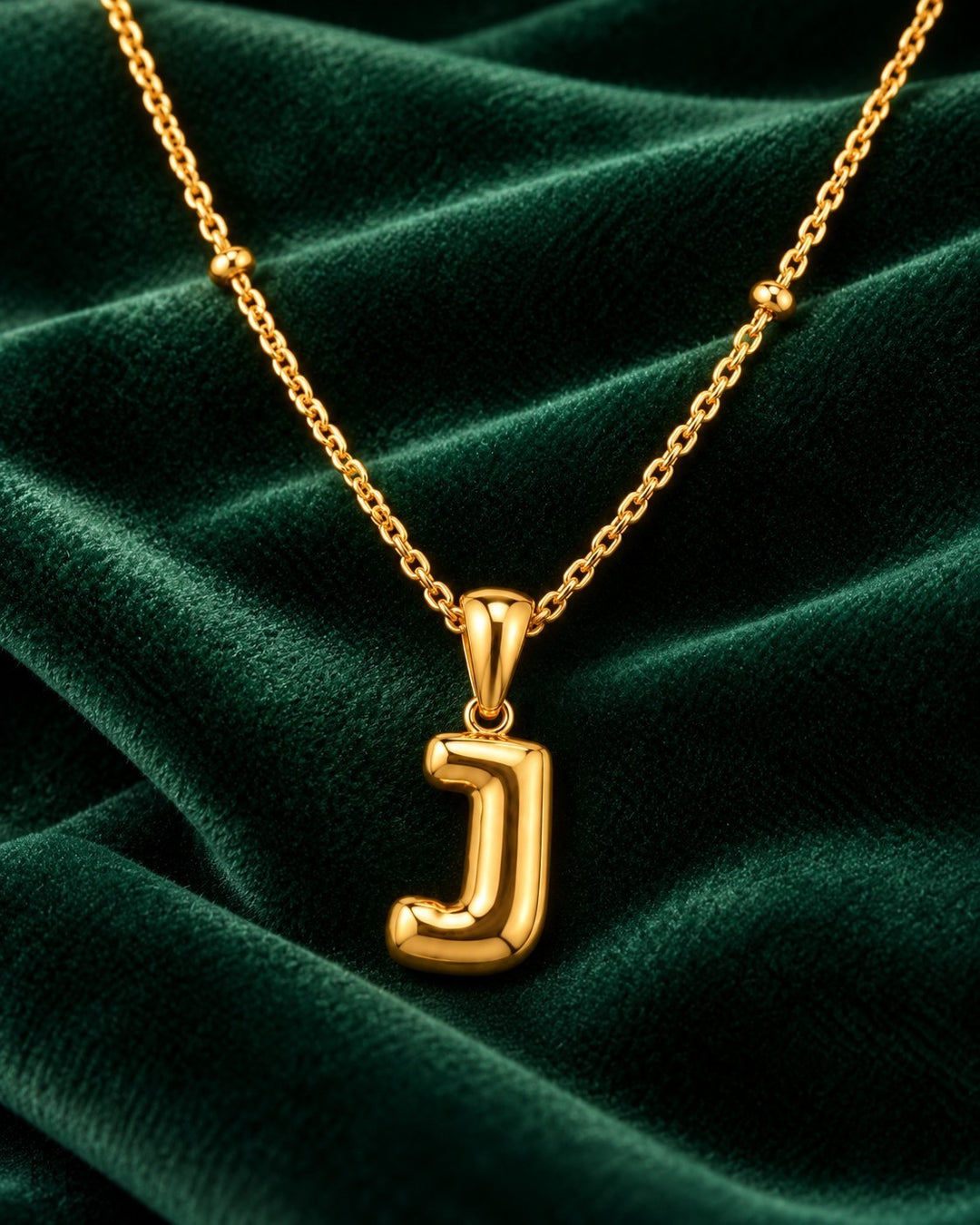 Elli Jewellery gold plated chunky letter J pendant necklace on a dark green velvet background