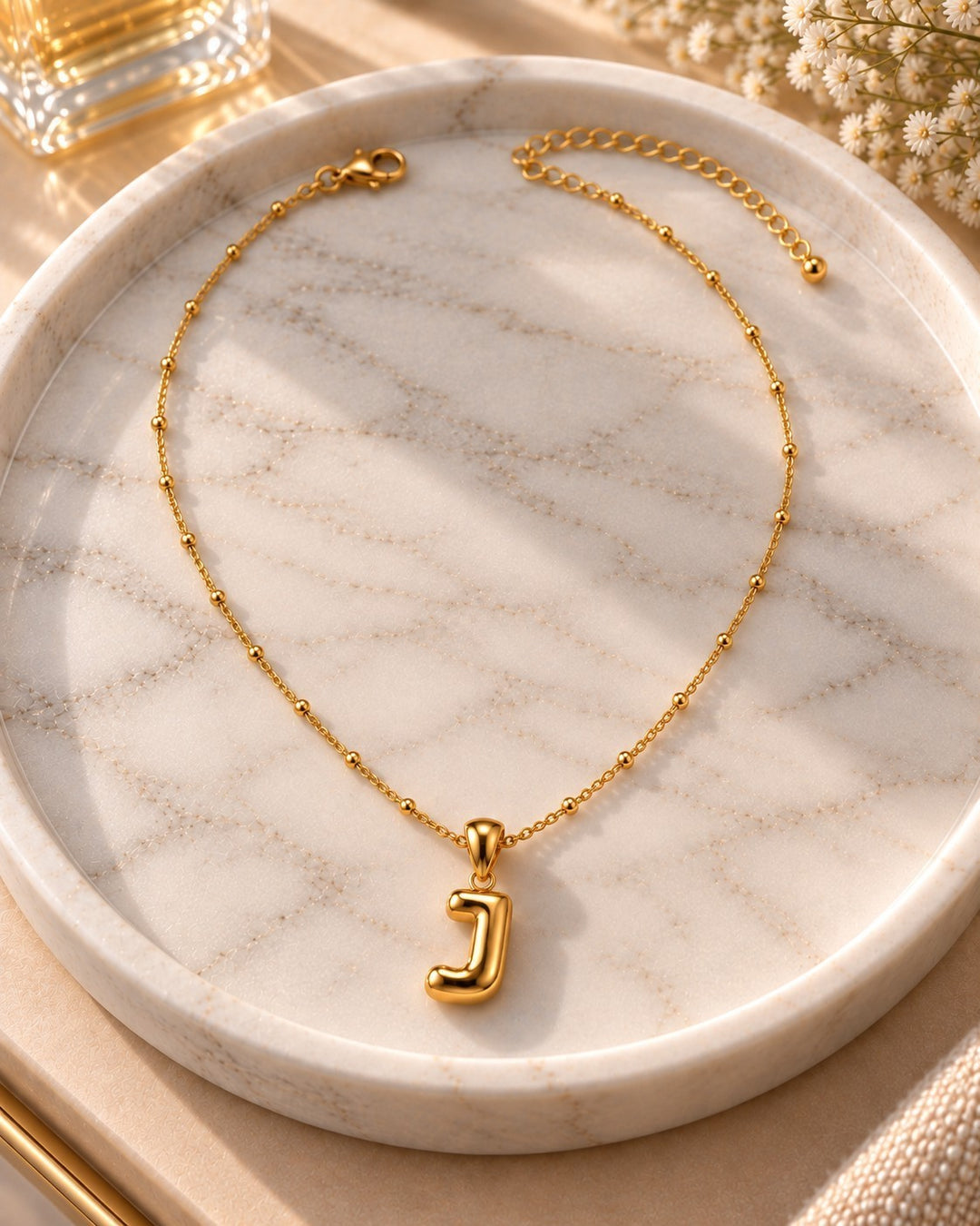 Elli Jewellery gold plated chunky letter J pendant necklace on a marble tray with delicate beaded chain detail.