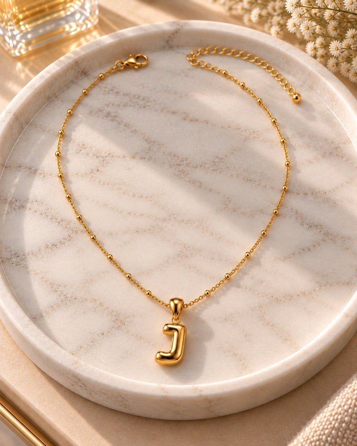 Elli Jewellery gold plated chunky letter J pendant necklace on a marble tray with delicate beaded chain detail.